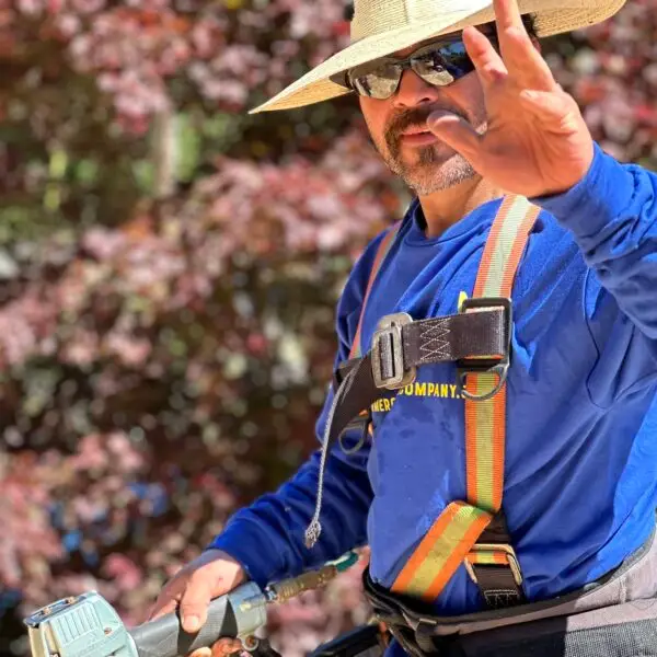 man in roofing uniform wearing a hat smiling and waving his hand at the camera