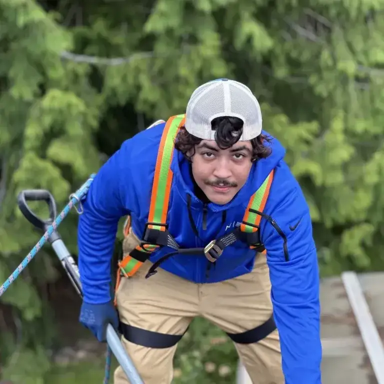 a roofer man in a blue jacket and white hat holding a rope