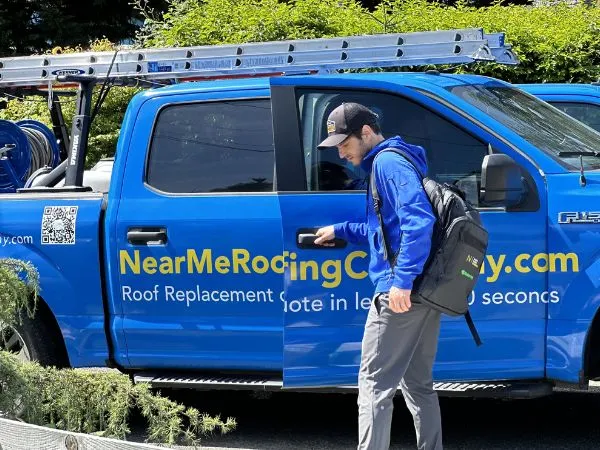 a man in a blue jacket and cap standing next to a blue roofing truck