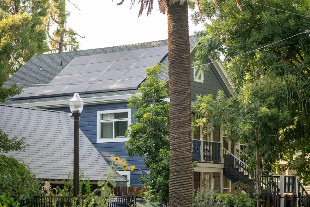 A blue house solar panels surrounded by trees and plants